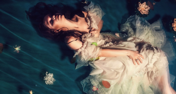woman in a gown clutching her collar against watery backdrop with flowers for romantic fantasy