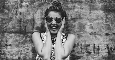 black and white photo of a girl laughing, holding her ears, wearing sunglasses