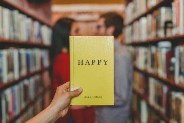 two people stand in a library behind a book entitled happy