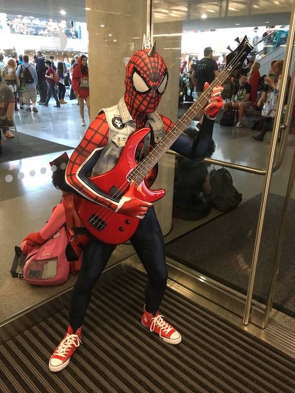A Spider-Man cosplayer with a denim vest covered in patches, a metal-spice mohawk, red converse, holding a red guitar