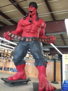 A towering red Incredible Hulk holds a Happy Halloween banner in front of bookshelves