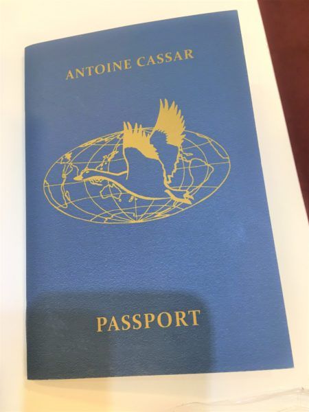 A blue pamphlet resembling a passport, with the text "Antoine Cassar" and an image of a bird over a globe
