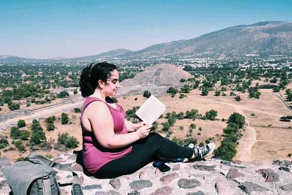A photo of me sitting and reading a book outdoors with a pyramid in the background