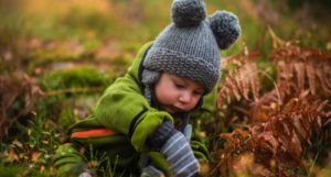 a small child in a gray knit hat playing outdoors in grass