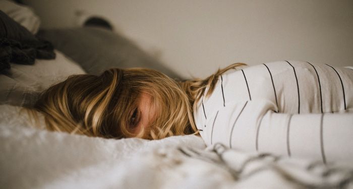 a photo of someone lying facedown on the bed, looking through their hair at the viewer