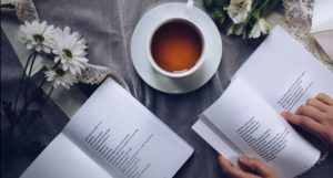 a cup of tea and flowers arranged next to two open books of poetry