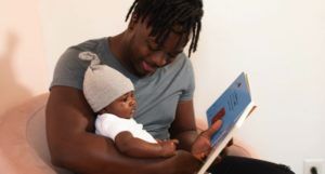 a photo of a Black father reading to a baby