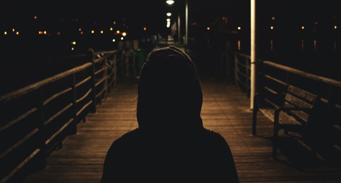 a hooded figure at night, seen from behind
