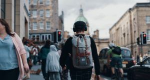 young person wearing a backpack and headphones walking down the street