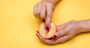 two hands holding half a peach, one finger pressing into where the pit would be