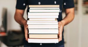 a person holding a stack of books https://www.pexels.com/photo/person-holding-stack-of-books-4218982/