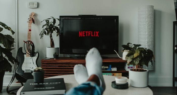 image of a black flat screen TV displaying the Netflix logo and a person's crossed legs https://unsplash.com/photos/yubCnXAA3H8