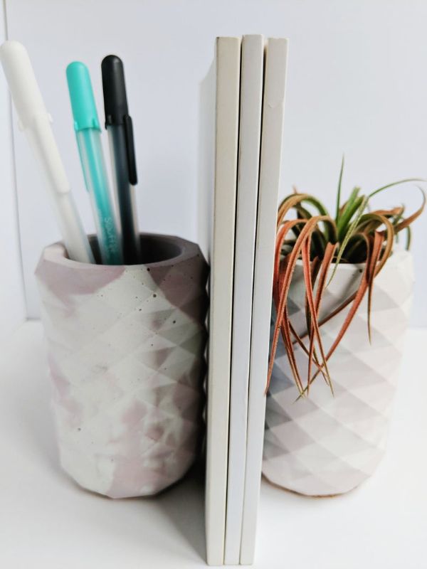 two geometric concrete vases used as bookends, one with pens in it and the other with a plant