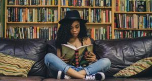 young adult teen woman reading a book in front of bookshelves feature 700x375