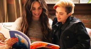 A transfeminine non-binary person and transmasculine gender-nonconforming person reading a magazine together