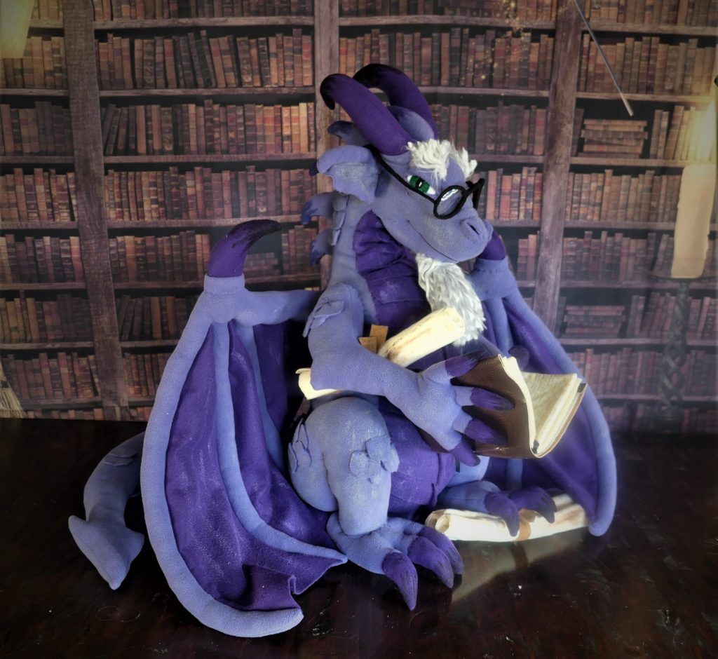 A fleece dragon toy holding scrolls and a book