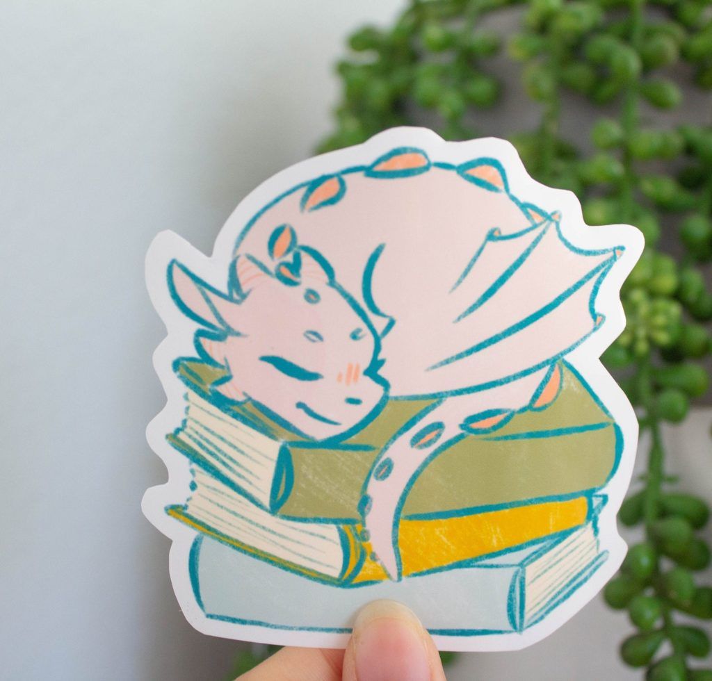 Sticker of an adorable dragon sleeping on a stack of books