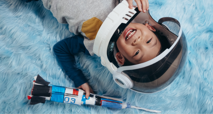little boy in astronaut helmet lying on a blue carpet and smiling