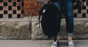 waist down photo of young person holding a black backpack wearing jeans and grey sneakers https://unsplash.com/photos/O0T1SIgHAfM