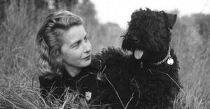 a black and white photo of Margaret Wise Brown with a black dog lying in a field