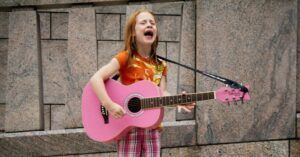 middle grade child singing and playing music on a pink guitar on the street