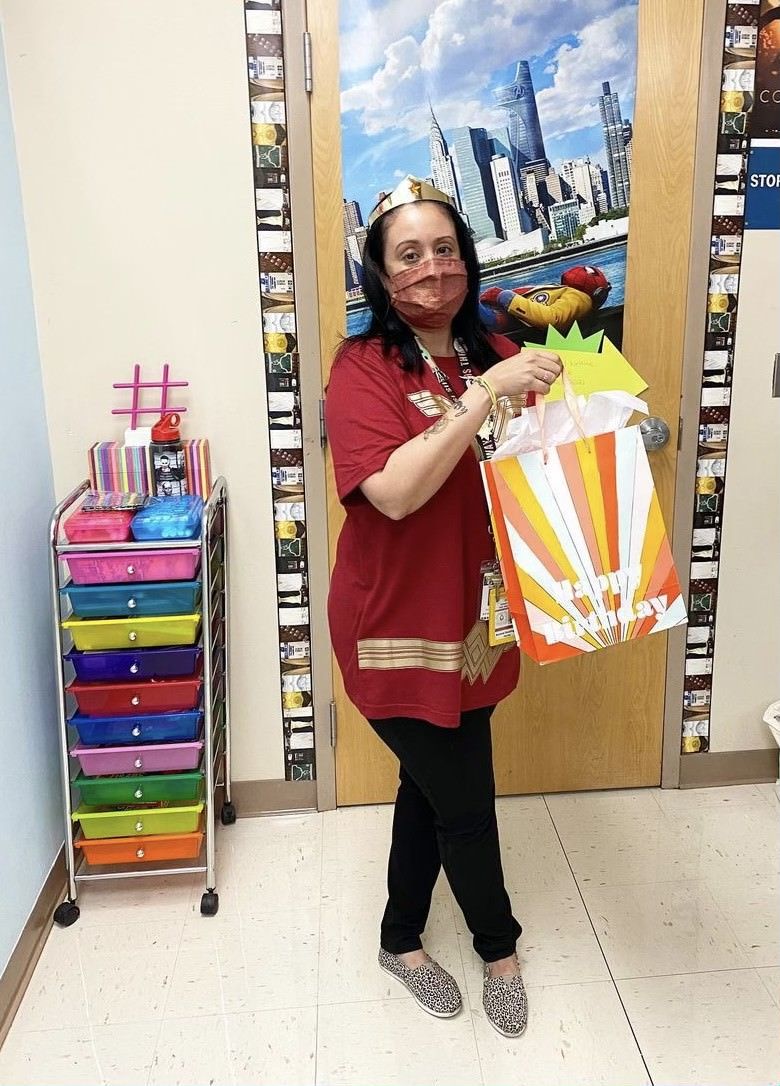 Aurora Dominguez in a Wonder Woman costume and a red face mask holding a birthday gift bag in her classroom at Boca Raton Community High Schoo