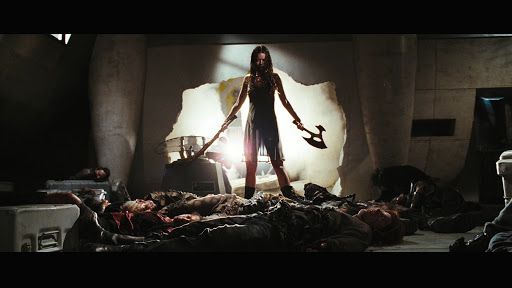 Still from Serenity (2005) of River Tam wielding weapons in each hand, standing over a pile of bodies
