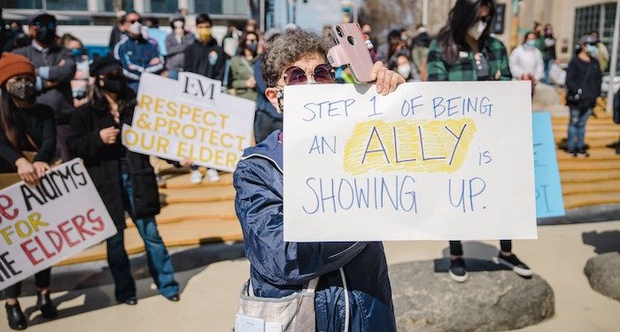 A photo of a protest sign reading "Step 1 of being an ally is showing up"