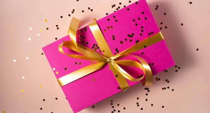 gift box in pink wrapping paper with gold ribbon and confetti