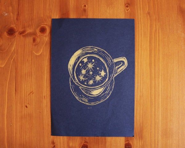 a navy blue print with gold teacup filled with stars sits on a wooden background