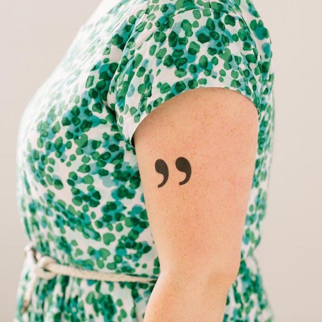 Image of a person’s torso and left arm. The left arm has a quotation marks temporary tattoo
