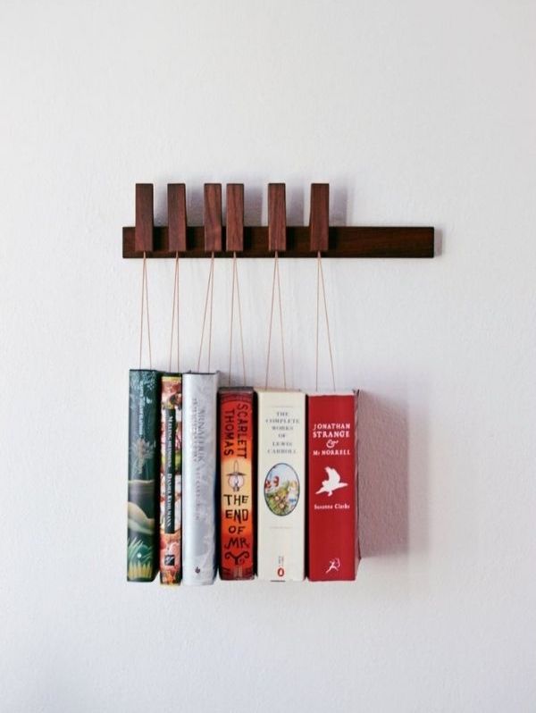 Hanging book rack with books hanging from string attached to pins on wooden ledge