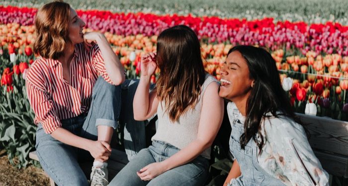 three young women laughing and sitting on a bench in a field of tulips https://unsplash.com/photos/cIfLUEZYLVg