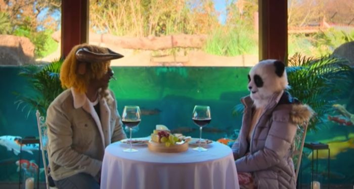 still frame from Netflix's SEXY BEASTS: two people sitting across from one another at a small white table, one dressed in a panda costume and the other as a bull