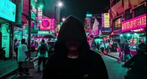 hooded figure in black colorful in colorful city at night