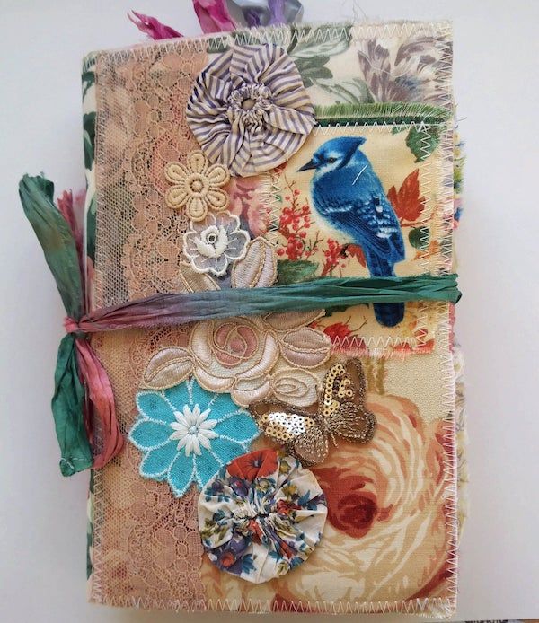 Junk journal with embellishments including blue bird and sequined butterfly.