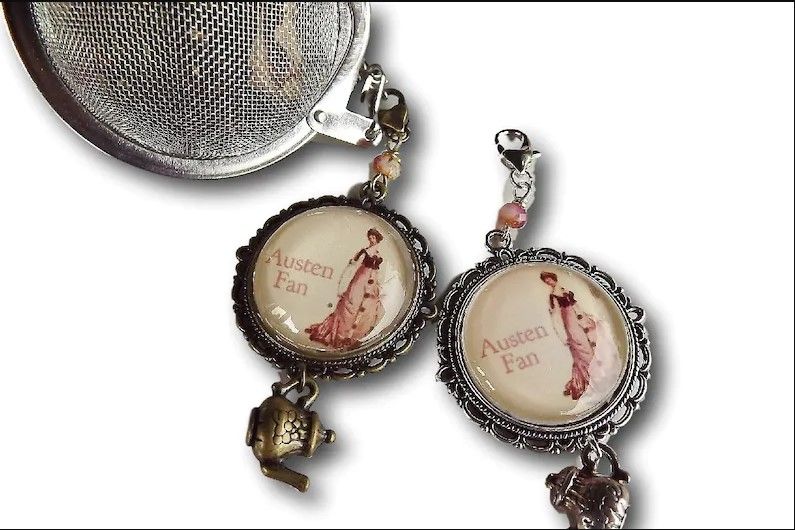 ball tea infuser with a bronze teapot charm and a cabochon with an image of a Georgian era girl with the text Austen fan on it