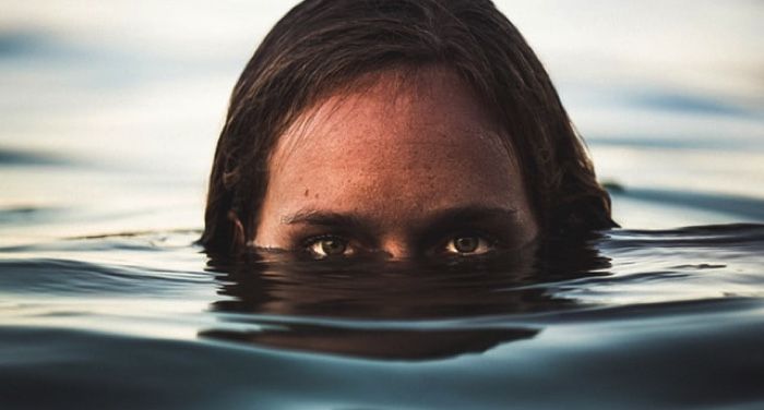 a person looks creepily with half of their face under water