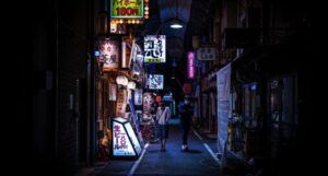creepy image of two people walking down a dark Japanese alleyway lit with neon signs