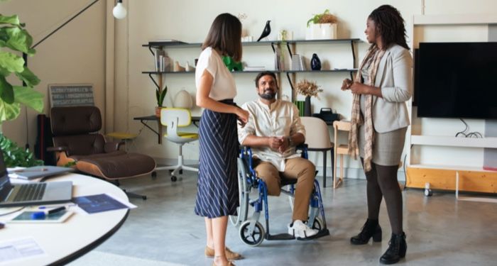 a team having a discussion in an office. Two women are standing, a man in a wheelchair is positioned between them