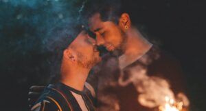 two men about two kiss holding a sparkler
