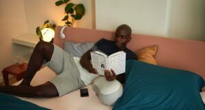Image of a Black man reading a book on a bed.