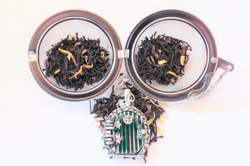 image of a ball style tea infuser with a green rounded hobbit door as a charm