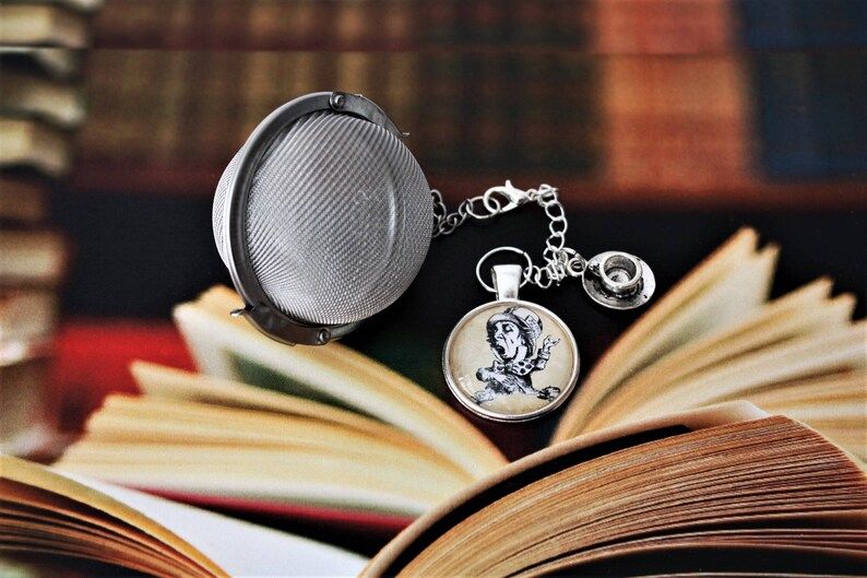 ball style tea infuser with a tea cup charm and a cabochon with an image of John Tenniel's Mad Hatter from Alice in Wonderland