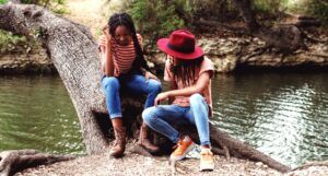 two young women sitting on a tree trunk by a body of water