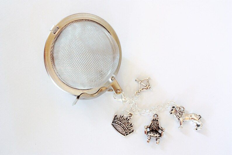 ball style tea infuser with charms of a crown, throne, lion, and bow and arrow, all silver.