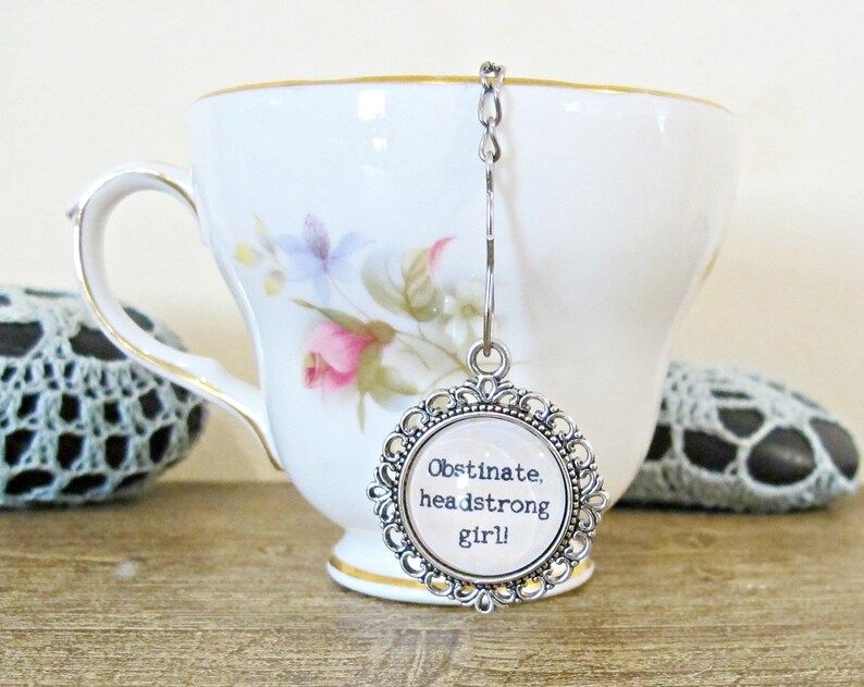 image of a pride and prejudice tea infuser in a white mug with the quote "obstinate headstrong girl" on the infuser charm