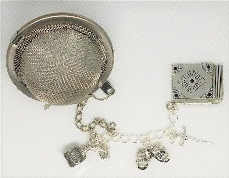ball tea infuser with a chain of silver charms: an ink pot with a quill in it; a set of theatre tragedy masks; a dagger; and a closed book.
