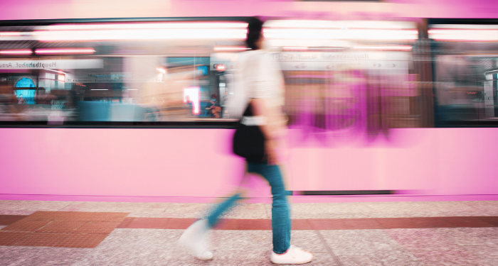 Blurred image of a woman in jeans walking alongside a moving subway car, tinted pink