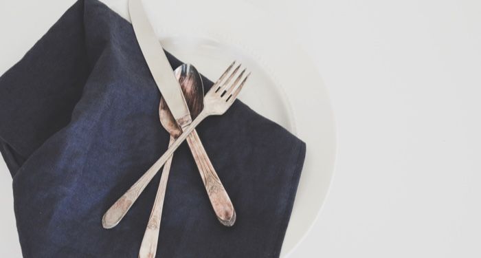 a silver fork, spoon, and knife resting on a blue napkin and white plate